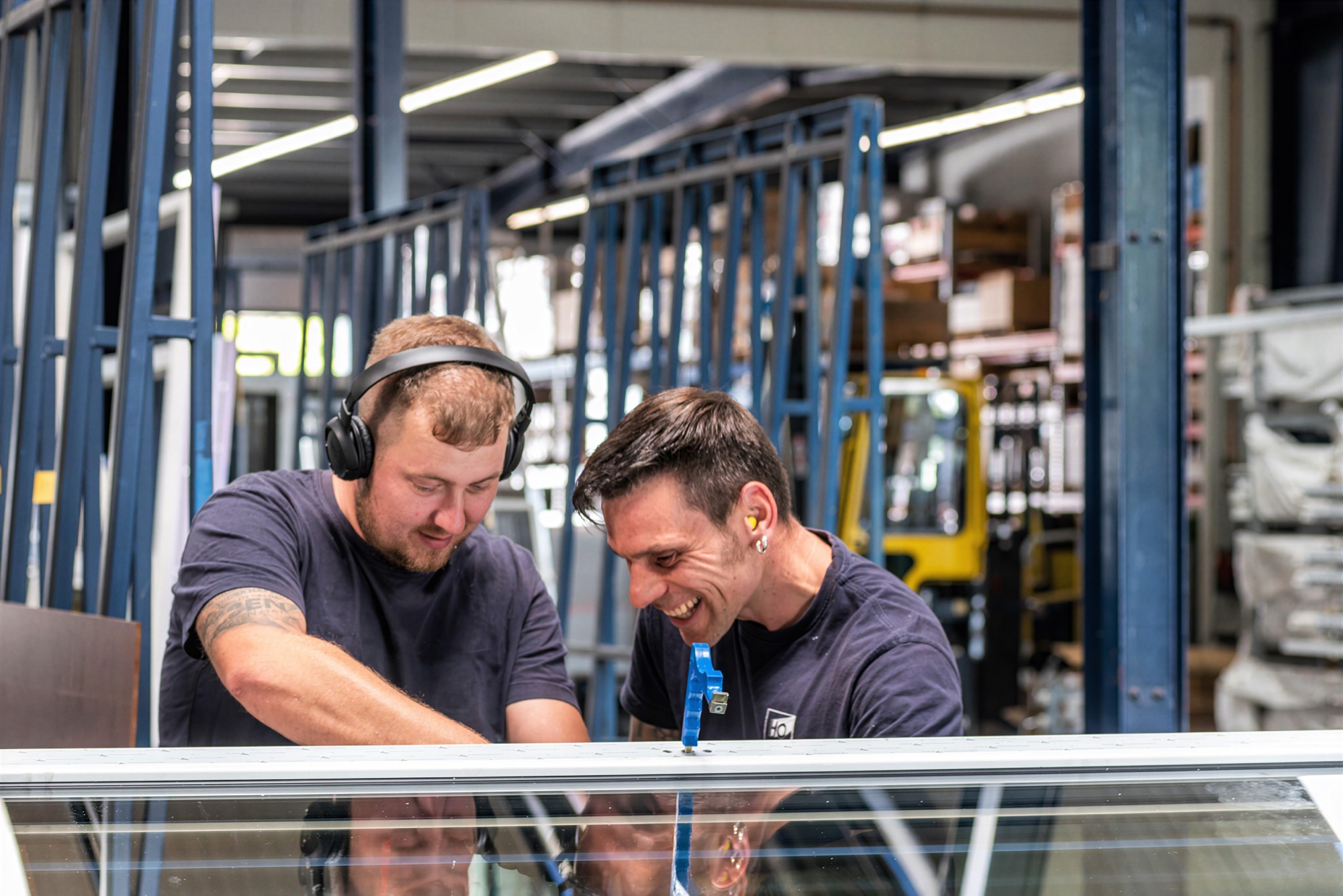 Zwei Mitarbeiter arbeiten in der Fertigungshalle gemeinsam an einem Fensterelement, einer von beiden lacht